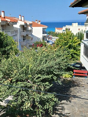 Zona residencial con vista despejada al mar, un camino pavimentado y un banco rojo.