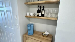 A room with a coffee maker, wine bottles, and glasses on shelves. - 204 Martinique in Ponce Inlet, FL (Ponce Inlet)