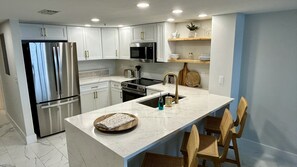 Una cocina moderna con electrodomésticos de acero inoxidable, encimera de mármol y barra de desayuno con sillas de mimbre.