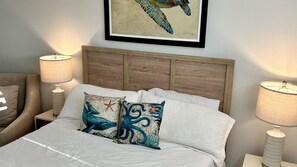 A neatly made bed with decorative pillows, a wooden headboard, and two bedside lamps. - 204 Martinique in Ponce Inlet, FL (Ponce Inlet)