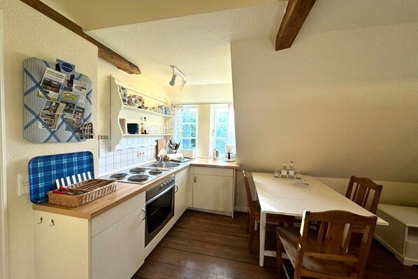 A compact kitchen with a central island, a dining table with chairs, and a window providing natural light. - Old registry office studio apartment (Oldsum)