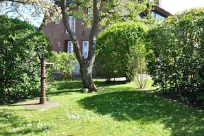A brick building with a garden area featuring a tree and a metal structure. - Old registry office studio apartment (Oldsum)