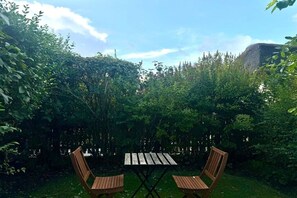An outdoor seating area with a wooden table and chairs, surrounded by dense foliage and a wooden fence. - Old registry office studio apartment (Oldsum)