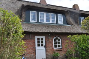 A traditional thatched-roof house with a brick facade, a white door, and a small window with a white frame. - Old registry office studio apartment (Oldsum)