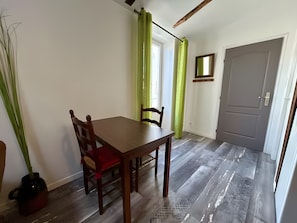 Een eetgedeelte met een houten tafel en stoelen, een kamerplant, een spiegel aan de muur en een deur op de achtergrond.