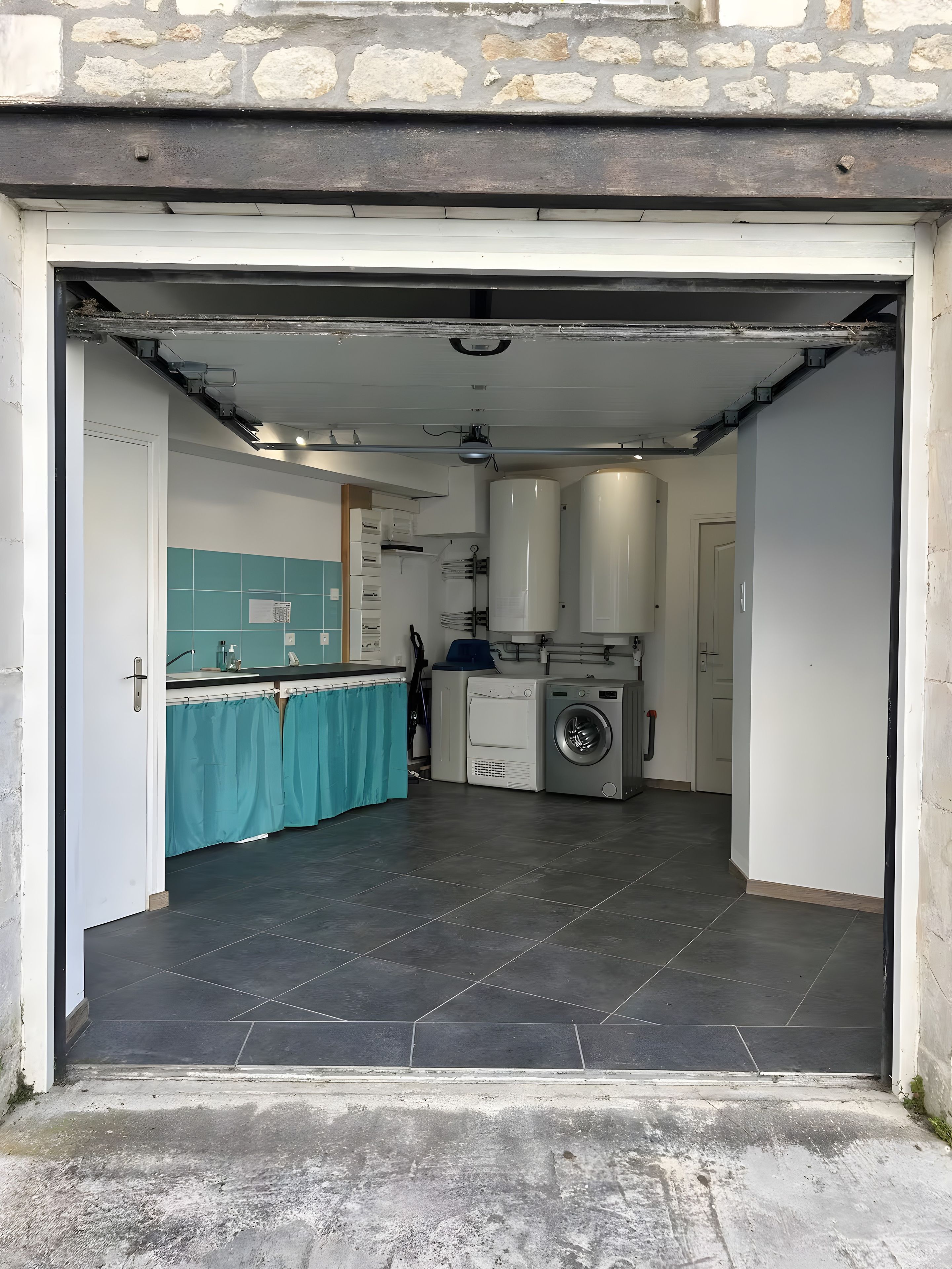An open garage leading to a kitchen with a washing machine, a sink, and a tiled floor.