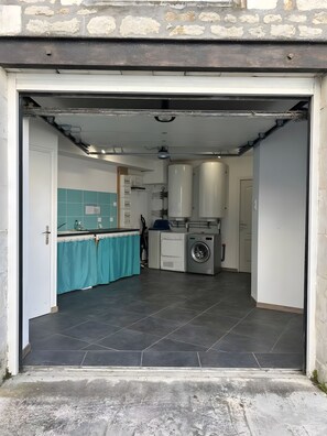 Een open garage die uitkomt op een keuken met een wasmachine, een spoelbak en een betegelde vloer.