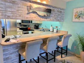 A modern kitchen with a bar area, stainless steel appliances, and a wooden accent wall. - #211 Curran Shores N.  Cozy 1/1 Condo Daytona Beach Shores (Daytona Beach Shores)