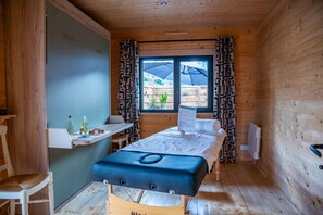 Una habitación pequeña y acogedora con una cama, un escritorio y una silla. Se ve una ventana con cortinas, y un radiador en la pared.