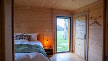 A wooden cabin bedroom with a bed, bedside table, and a view of the outdoors.