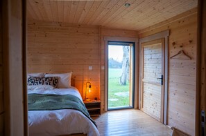 A wooden cabin bedroom with a bed, bedside table, and a view of the outdoors.