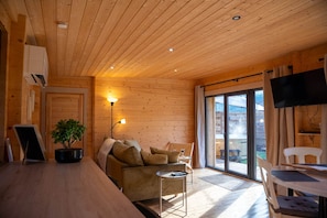 L’intérieur chaleureux d’un chalet avec un plafond en bois, un canapé, une petite table, une plante en pot et une porte-fenêtre coulissante donnant sur un espace extérieur.
