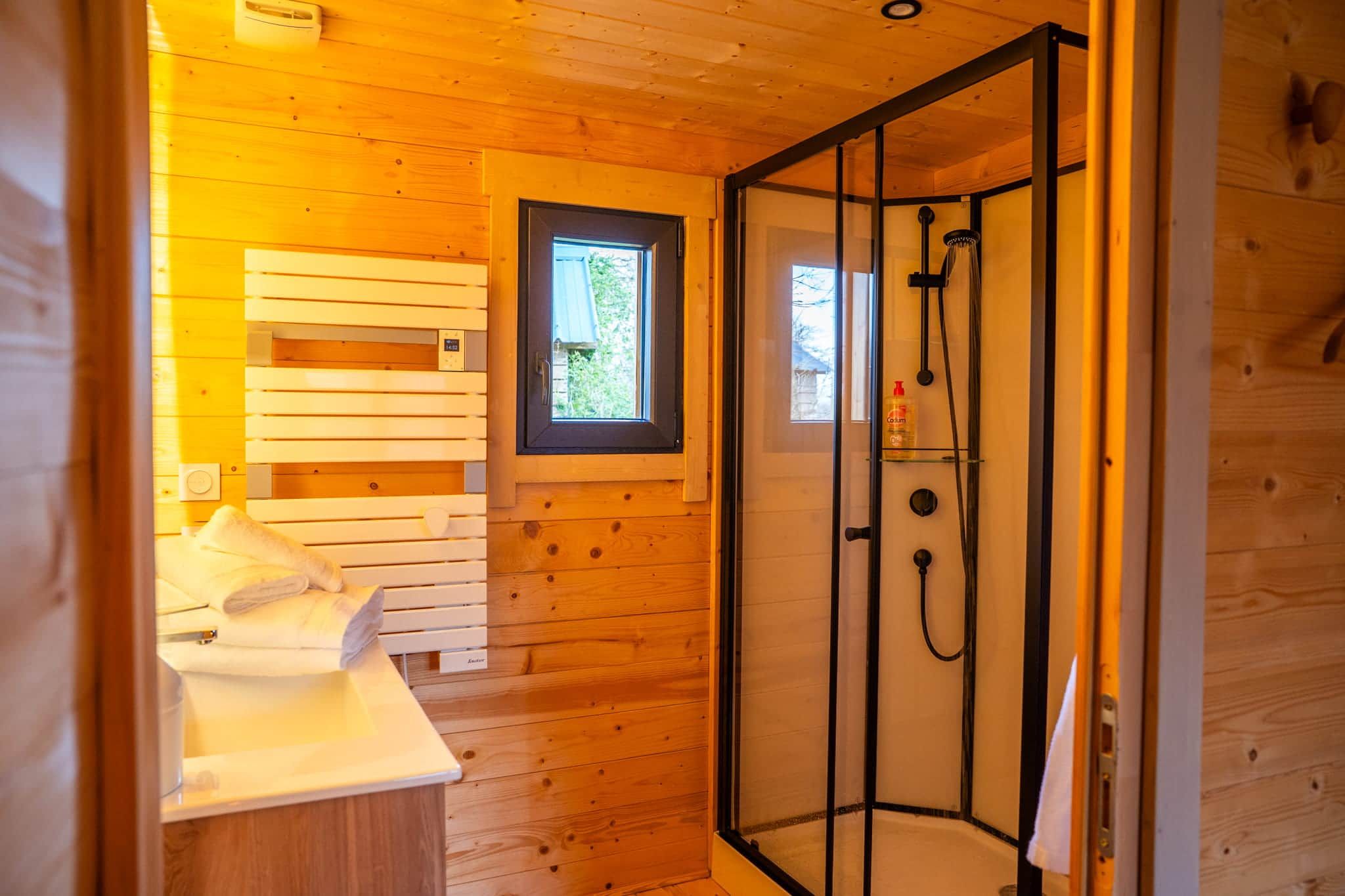 Ein Holzblockbau-Innenraum mit Dusche, Fenster und einem Bett mit Handtüchern.