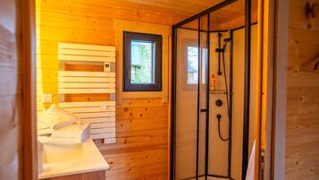 Ein Holzblockbau-Innenraum mit Dusche, Fenster und einem Bett mit Handtüchern.