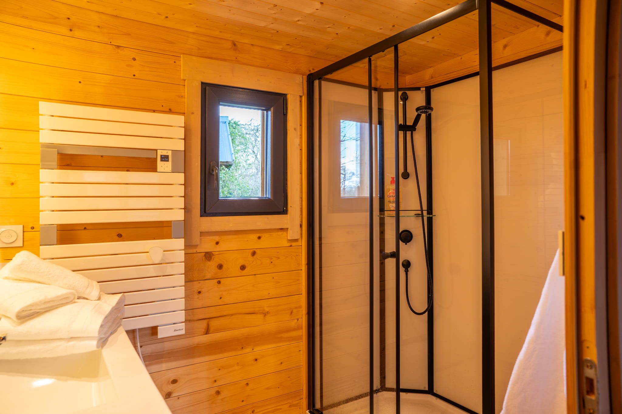 Une salle de bain rustique, aménagée dans une cabane en bois, avec une douche, une fenêtre et un porte-serviettes.