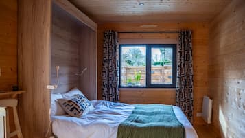 Een slaapkamer in een houten blokhut met een bed, gordijnen, een raam en een radiator.