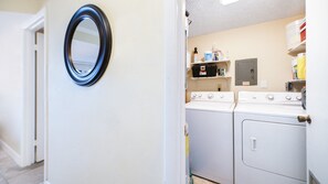 A laundry room with a washing machine, dryer, and a shelf with cleaning supplies. - #212 Sandcastle 2/2 Oceanfront Traffic Free Beach (Ponce Inlet)