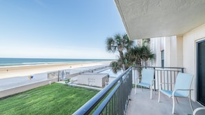 A balcony with a view of the beach, a small lawn, and a few chairs. - #212 Sandcastle 2/2 Oceanfront Traffic Free Beach (Ponce Inlet)