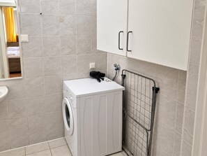 Een kleine wasruimte met een wasmachine, een droogrek en een wit kastje.