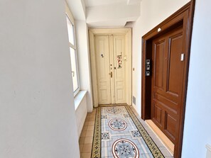Um corredor com piso ladrilhado, uma porta branca e uma porta marrom.