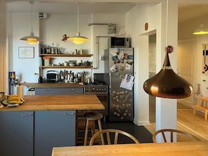 A modern kitchen with a central island, bar stools, and a hanging pendant light. - Light and spacious flat in Nørrebro with garden (København)