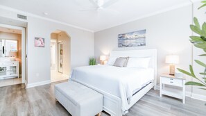 Un dormitorio con cama, mesitas de noche, un banco y un cuadro en la pared.