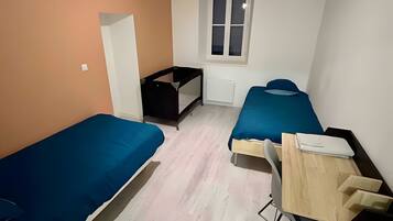 Une petite pièce, de taille modeste, comprenant deux lits simples, un bureau avec une chaise, un radiateur et une fenêtre.