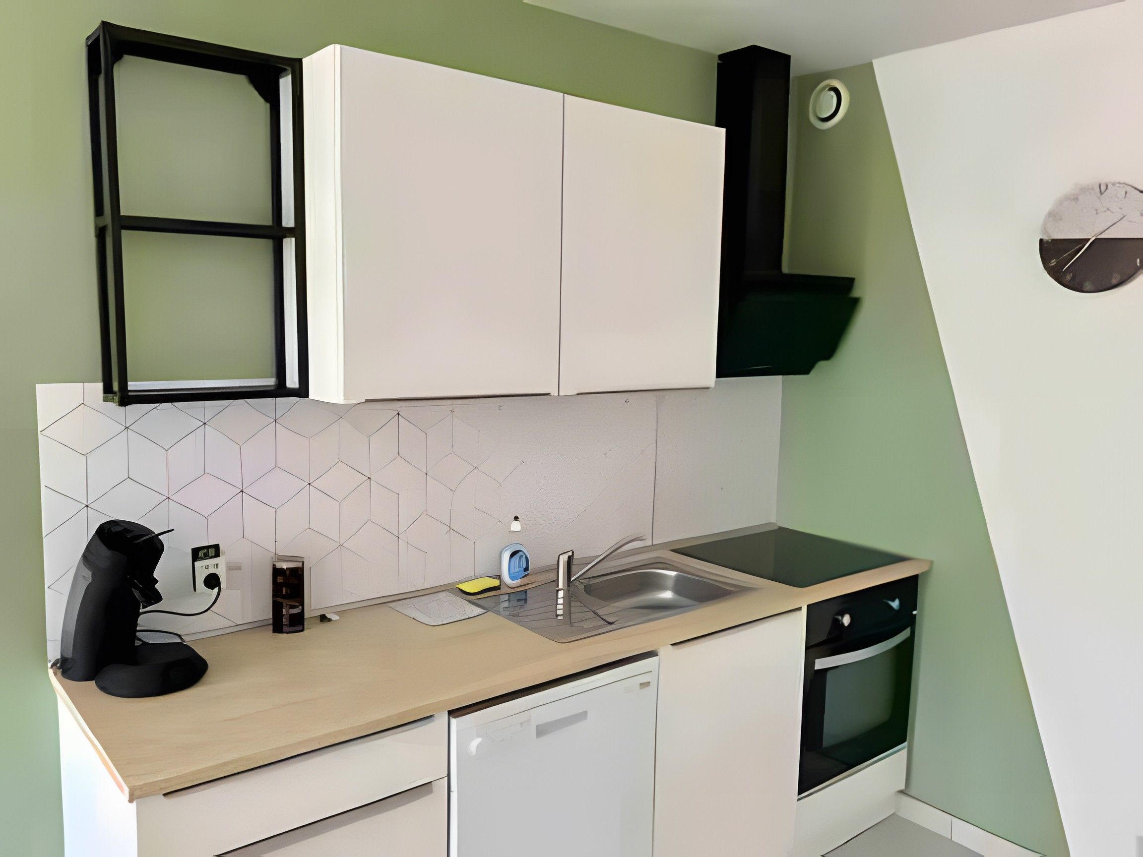 Une cuisine de taille réduite avec des meubles blancs, un lave-vaisselle, un évier et une cuisinière.