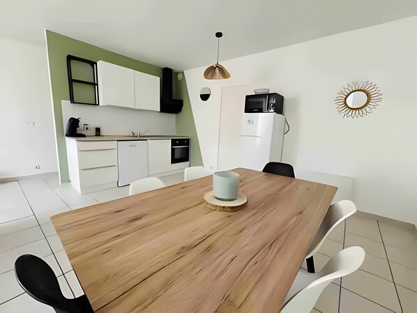 Une cuisine moderne avec des meubles blancs, une table à manger en bois et un four à micro-ondes.