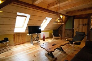 A cozy room with wooden walls, a wooden floor, a table, a chair, a television, and two skylights. - Holiday apartment with 1 bedroom (Rockow)