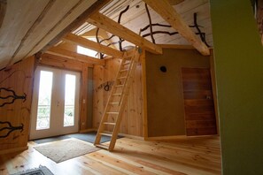 A wooden interior with a ladder leading to a loft area, a door to an outdoor space, and a small window. - Holiday apartment with 1 bedroom (Rockow)