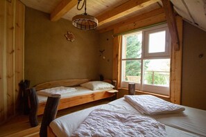 Een houten kamer met twee bedden, een raam met uitzicht op groen en een hanglamp.