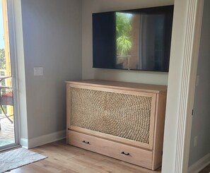 Een kamer met een houten kast, een aan de muur bevestigde televisie en een schuifdeur naar een buitenruimte.