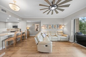 A modern kitchen with a central island, a dining area with chairs, a large beige sectional sofa, and a ceiling fan. - 2306 Harbour Village (Ponce Inlet)