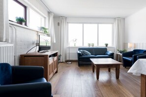 Ein modernes Wohnzimmer mit einer Couch, Sesseln, einem Couchtisch und einem Fernseher auf einer Holzkommode.
