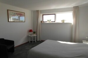 Ein Hotelzimmer mit einem Bett, einem kleinen Tisch mit Lampe, einem Stuhl, einem Fenster mit Vorhängen und einem gerahmten Bild an der Wand.