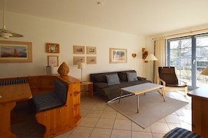 A living room with a sofa, a wooden bench, a coffee table, and a chair. There are framed pictures on the wall and a lamp. - Oak Park W 4.2||Ostseebad Prerow (Ostseebad Prerow)