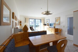 A dining area with a wooden table and benches, a television, and a window with curtains. - Oak Park W 4.2||Ostseebad Prerow (Ostseebad Prerow)