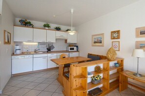 A compact kitchen with white cabinets, a wooden dining table, and a built-in bench. - Oak Park W 4.2||Ostseebad Prerow (Ostseebad Prerow)