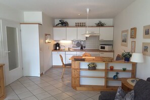 A compact kitchen with white cabinets, a microwave, and a dining area with a wooden table and chairs. - Oak Park W 4.2||Ostseebad Prerow (Ostseebad Prerow)