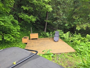 A wooden deck with a reclining chair and a small table, surrounded by dense green foliage. - Country house with rustic charm. Tastefully decorated. Photos available upon request (Saint-Sauveur)