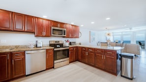 A modern kitchen with wooden cabinets, stainless steel appliances, and a view to the outside. - #305 Blue Surf 2/2 Oceanfront Traffic Free Beach (Daytona Beach Shores)