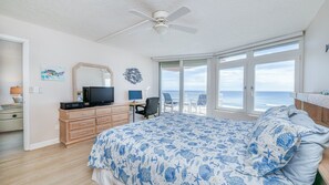 Une chambre à coucher comprenant un lit, un bureau, une chaise, un téléviseur et une grande fenêtre donnant sur l’océan.