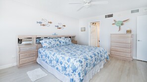 A bedroom with a bed, two nightstands, a dresser, a ceiling fan, and wall decorations. - #305 Blue Surf 2/2 Oceanfront Traffic Free Beach (Daytona Beach Shores)