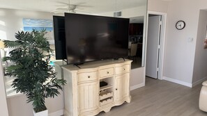 A living room with a flat-screen TV on a cabinet, a plant, and a dining area visible through an open door. - #305 Blue Surf 2/2 Oceanfront Traffic Free Beach (Daytona Beach Shores)