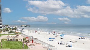 A beach with a pier, sun loungers, umbrellas, and a grassy area. - #305 Blue Surf 2/2 Oceanfront Traffic Free Beach (Daytona Beach Shores)