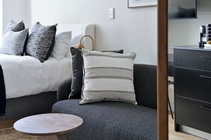 Ett modernt sovrum med en säng, en grå soffa, ett litet runt bord och en svart byrå.