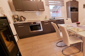 A modern kitchen with built-in appliances, a dining area with a table and chairs, and a window providing natural light. - Thatched house "Aenna" (Zierow)