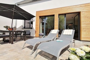 A patio with two lounge chairs, a table, and an umbrella. - Rosehip, Domizil am Ostseewald (Zingst)