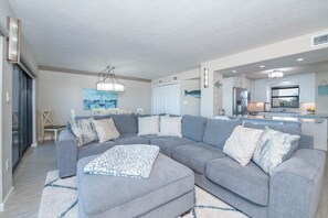 A modern living room with a grey sectional sofa, a patterned throw, and a kitchen area in the background. - #305 Sandcastle Oceanfront 3/2 Traffic Free Beach Ponce Inlet (Ponce Inlet)